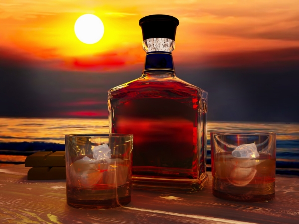 Zwei Gläser mit braunen Rum + einer großen Flasche dazu im Hintergrund das Meer der Karibik